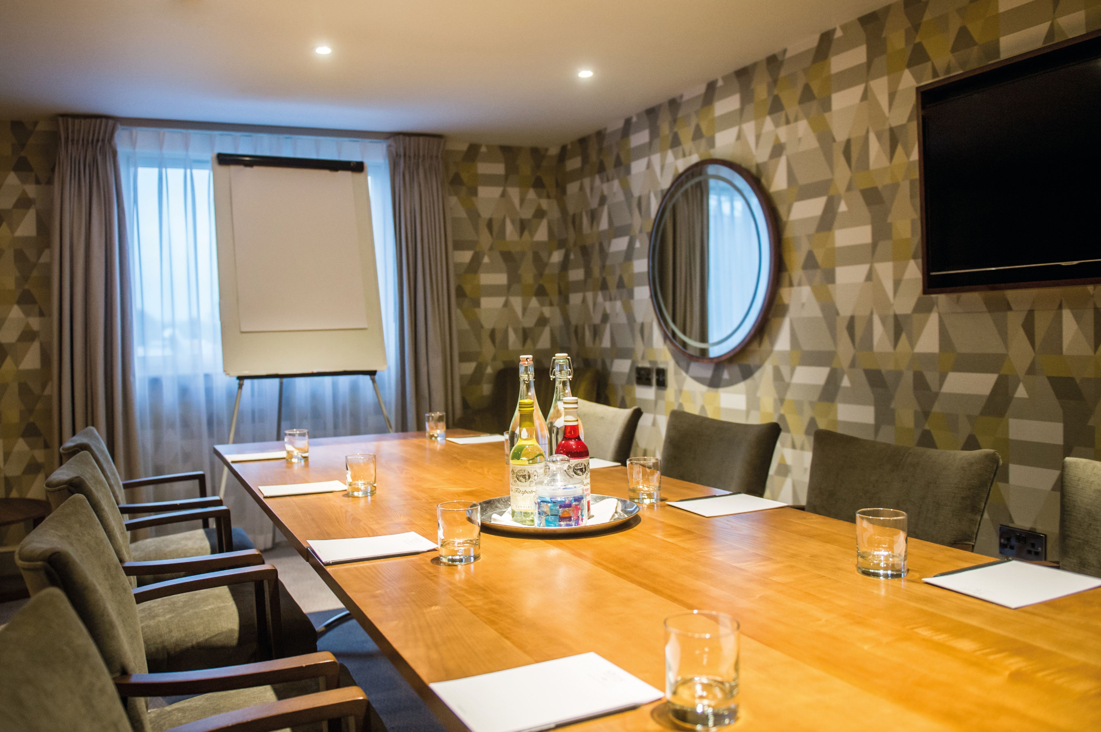 A meeting room with a flip chart, screen, mirror and a selection of drinks