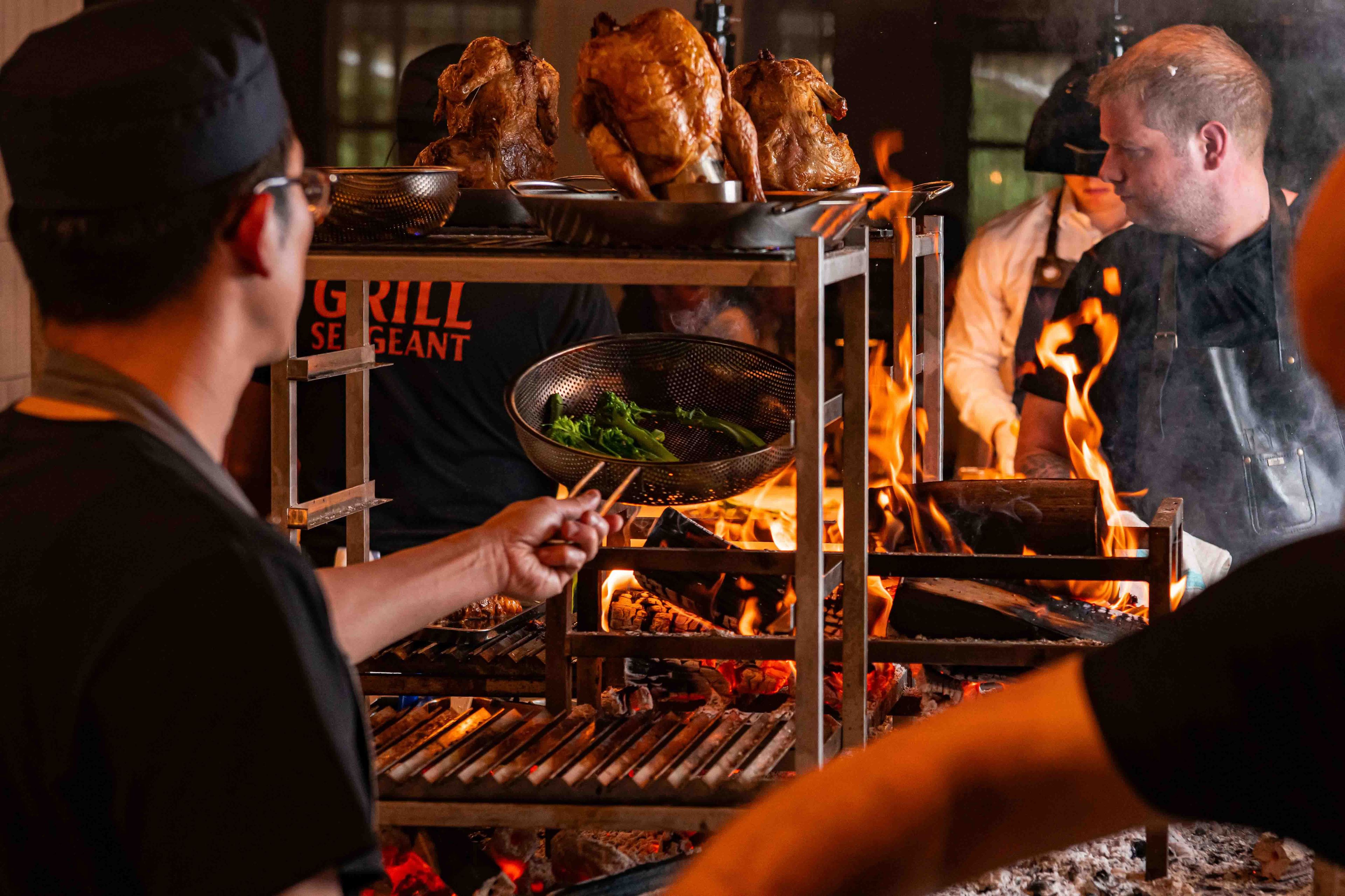 Chef cooking broccoli and roasting chicken on a open FYR grill